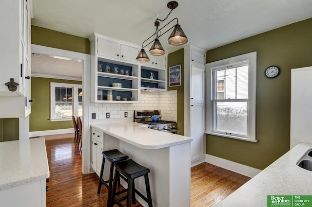 kitchen featuring baseboards, stainless steel range with gas cooktop, dark wood-type flooring, white cabinetry, and backsplash