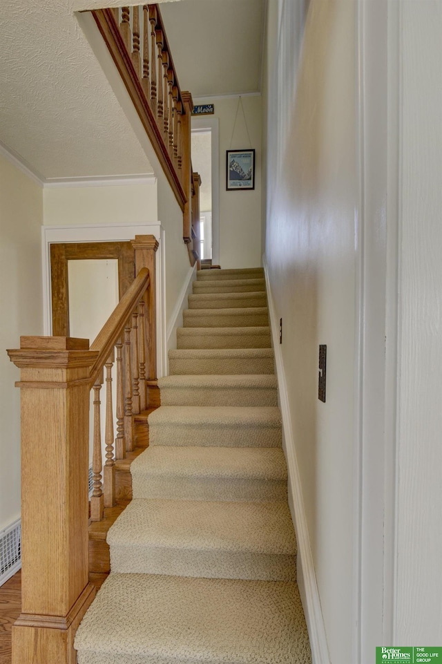 stairs with ornamental molding, visible vents, baseboards, and a textured ceiling