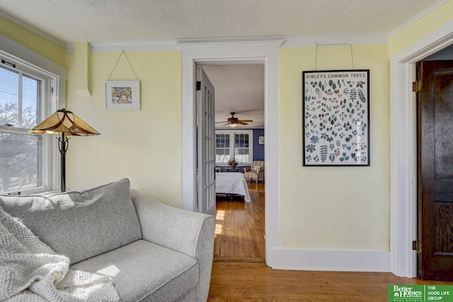 sitting room with a ceiling fan, wood finished floors, baseboards, a textured ceiling, and crown molding