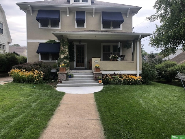 american foursquare style home with stucco siding, a porch, and a front yard