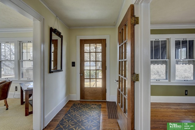 doorway with visible vents, baseboards, wood finished floors, and crown molding