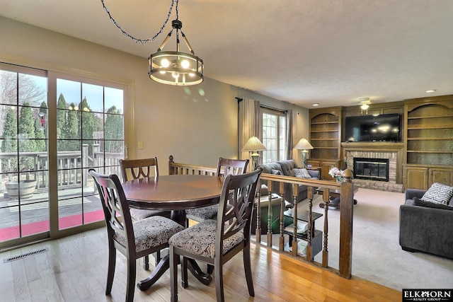 dining room with built in features, visible vents, a fireplace, and light wood finished floors