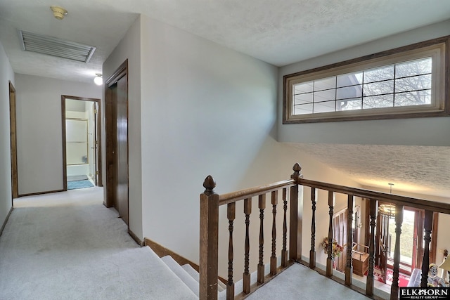 hall with visible vents, baseboards, carpet floors, an upstairs landing, and a textured ceiling