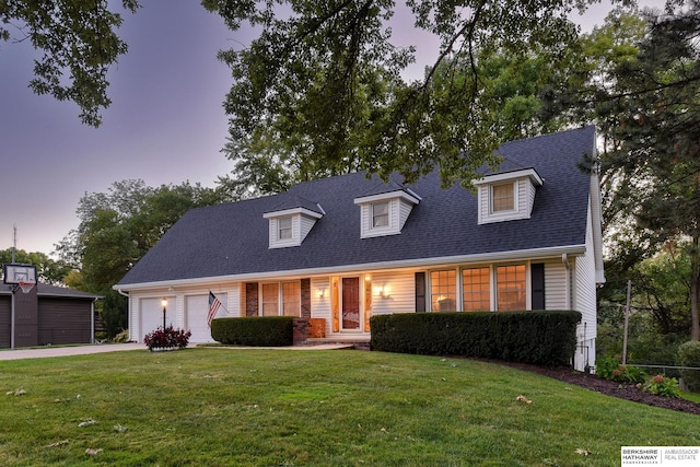 cape cod house with an attached garage, concrete driveway, a yard, and a shingled roof