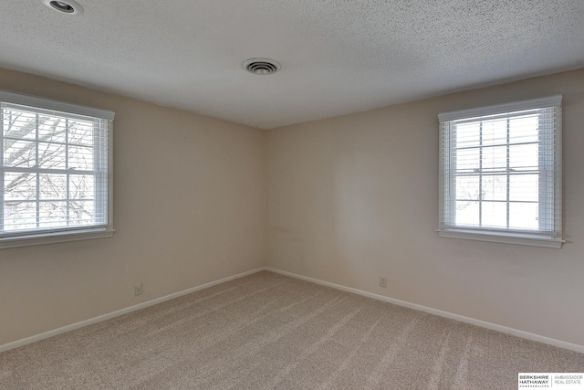 carpeted spare room featuring visible vents, baseboards, and a textured ceiling