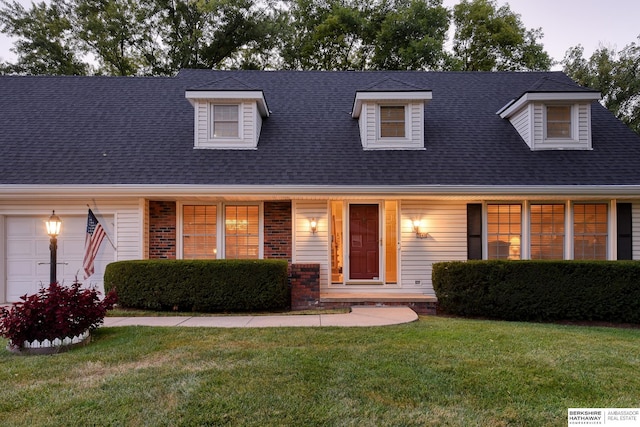 new england style home featuring brick siding, a shingled roof, a front lawn, covered porch, and an attached garage