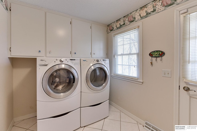 clothes washing area with a textured ceiling, washing machine and dryer, cabinet space, light tile patterned floors, and baseboards