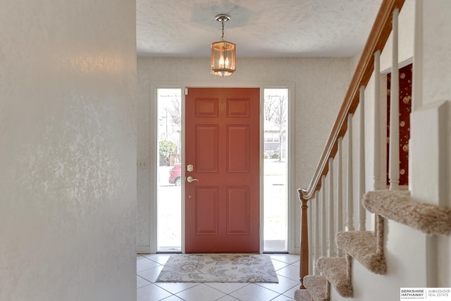 foyer featuring stairway, light tile patterned floors, a textured wall, and a textured ceiling