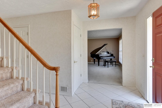 foyer entrance featuring visible vents, light carpet, a textured ceiling, light tile patterned flooring, and stairs