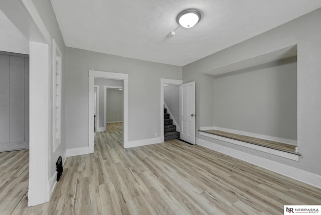 unfurnished living room featuring baseboards, a textured ceiling, wood finished floors, and stairs