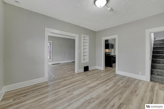 unfurnished living room with baseboards, a textured ceiling, stairs, and light wood finished floors