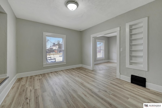 unfurnished room featuring built in features, a textured ceiling, baseboards, and light wood-style floors