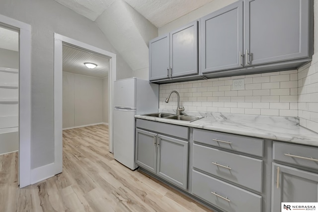 kitchen featuring light wood-type flooring, gray cabinets, a sink, freestanding refrigerator, and decorative backsplash