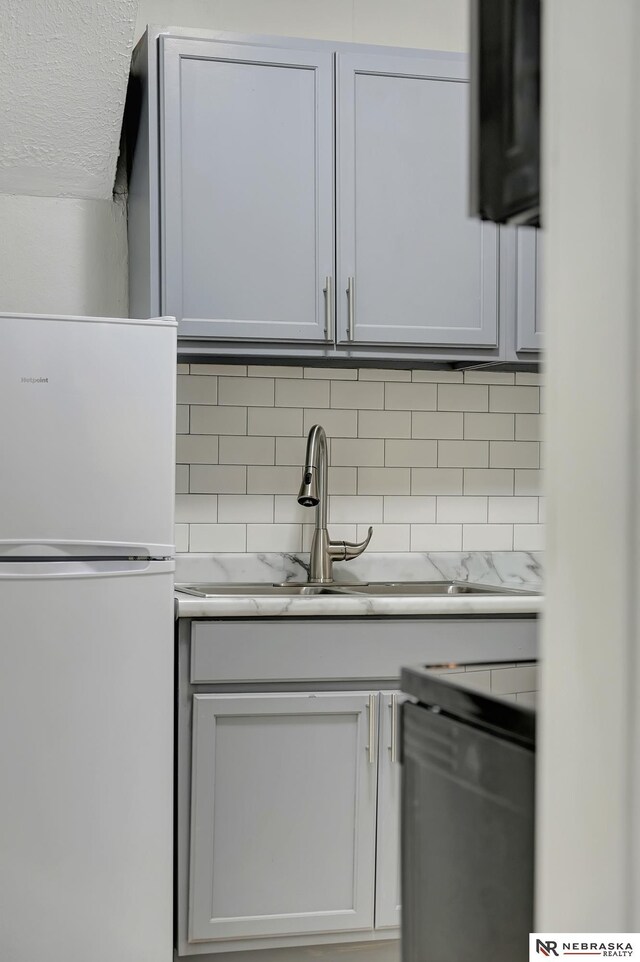 kitchen featuring dishwasher, tasteful backsplash, freestanding refrigerator, and a sink