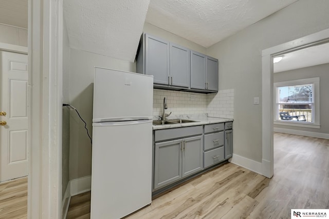 kitchen with gray cabinets, a sink, freestanding refrigerator, light wood-style floors, and decorative backsplash