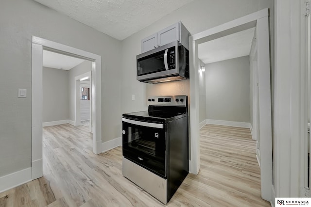 kitchen with stainless steel microwave, baseboards, light wood-style floors, electric range, and a textured ceiling