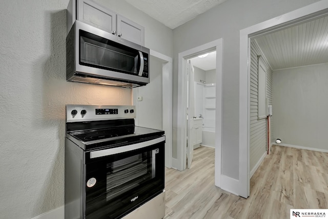 kitchen with baseboards, appliances with stainless steel finishes, light wood-style flooring, and a textured wall