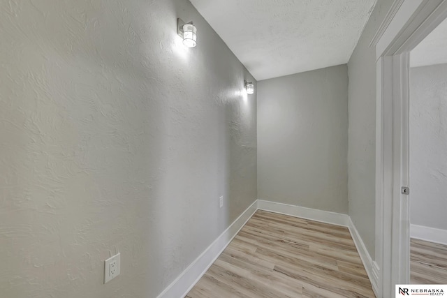 hallway with baseboards, light wood finished floors, and a textured ceiling