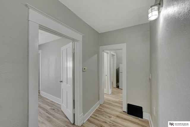 corridor featuring a textured wall, baseboards, and light wood finished floors