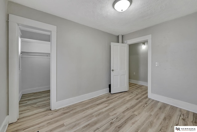 unfurnished bedroom featuring light wood-style flooring, baseboards, and a textured ceiling