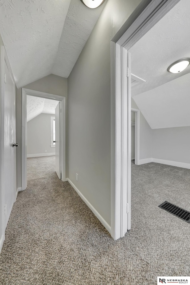 hall featuring visible vents, a textured ceiling, carpet floors, baseboards, and vaulted ceiling