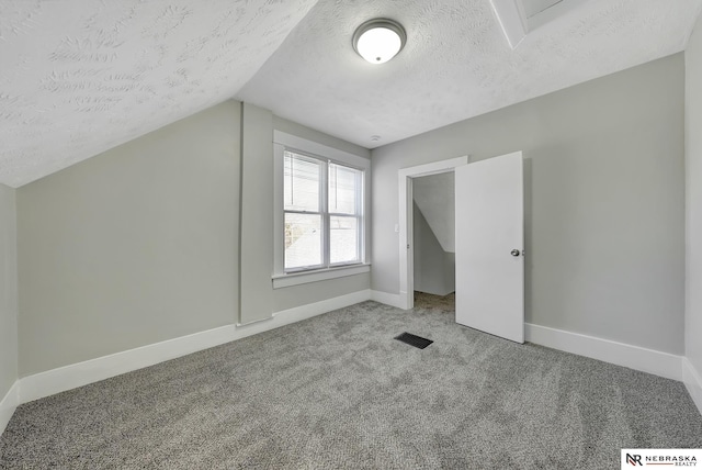 additional living space with carpet, baseboards, visible vents, vaulted ceiling, and a textured ceiling