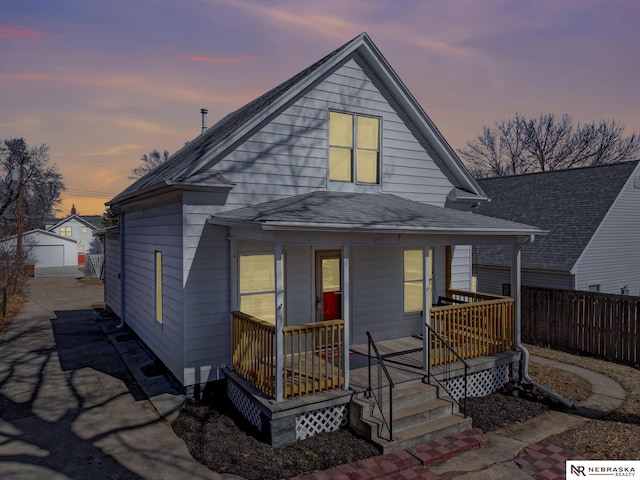 view of front of property featuring a porch, a shingled roof, an outdoor structure, and fence