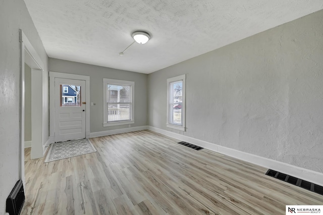 foyer featuring visible vents, a textured ceiling, light wood finished floors, baseboards, and a textured wall