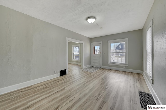 interior space featuring wood finished floors, visible vents, a textured wall, and baseboards