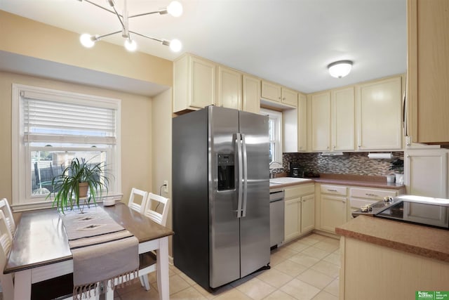 kitchen with backsplash, cream cabinets, appliances with stainless steel finishes, and light tile patterned flooring