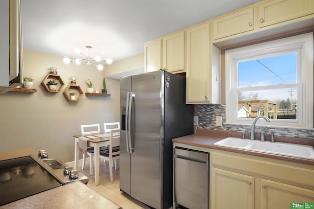 kitchen with backsplash, light tile patterned floors, cream cabinets, stainless steel appliances, and a sink