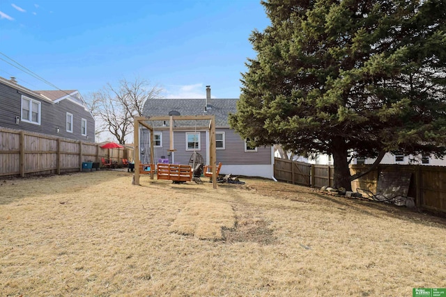 back of house with a lawn, a fenced backyard, and roof with shingles