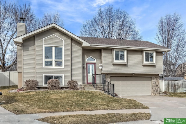 bi-level home with fence, an attached garage, a chimney, concrete driveway, and brick siding