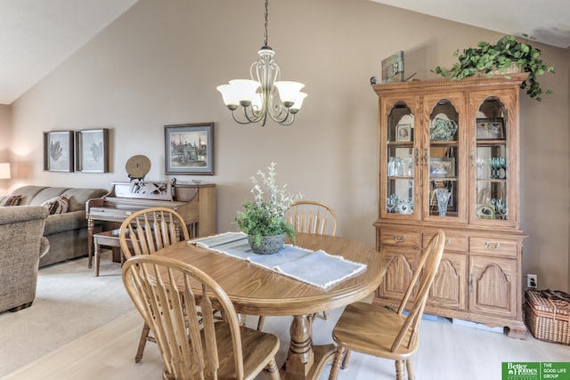 dining space with light wood finished floors, a notable chandelier, and vaulted ceiling