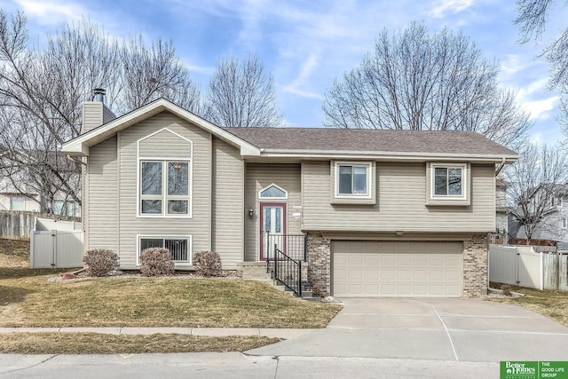 split foyer home featuring driveway, a gate, fence, a garage, and a chimney