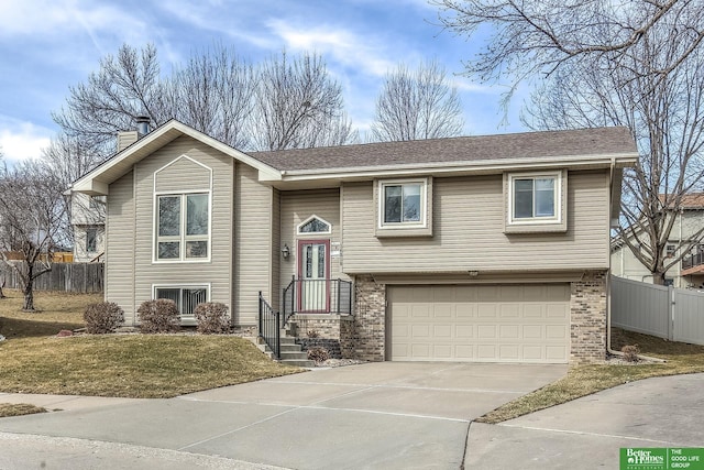 split foyer home featuring brick siding, concrete driveway, a chimney, and fence