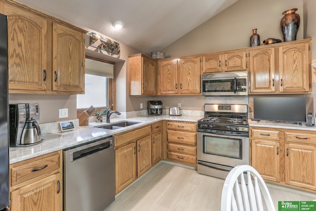 kitchen with light stone countertops, light wood-type flooring, vaulted ceiling, appliances with stainless steel finishes, and a sink