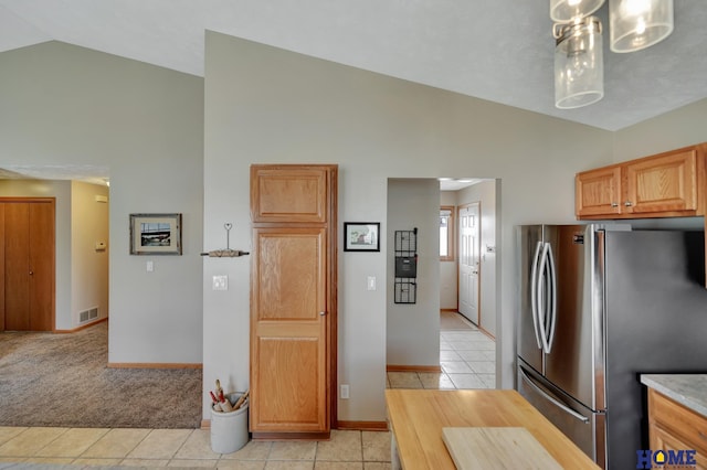 kitchen featuring visible vents, light carpet, freestanding refrigerator, light tile patterned flooring, and vaulted ceiling