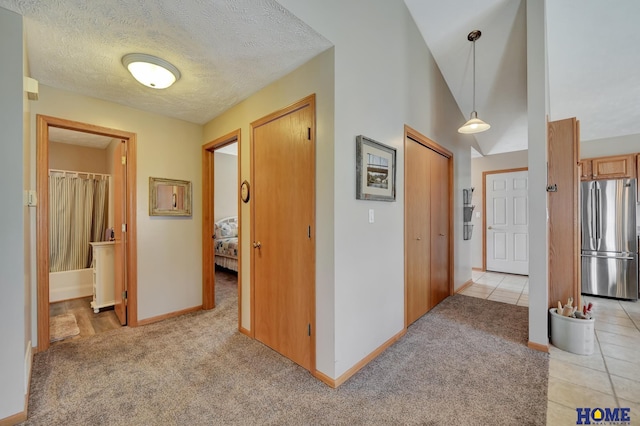 hallway with lofted ceiling, light colored carpet, baseboards, and a textured ceiling