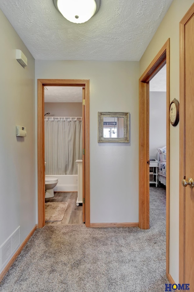 corridor with visible vents, baseboards, carpet, and a textured ceiling