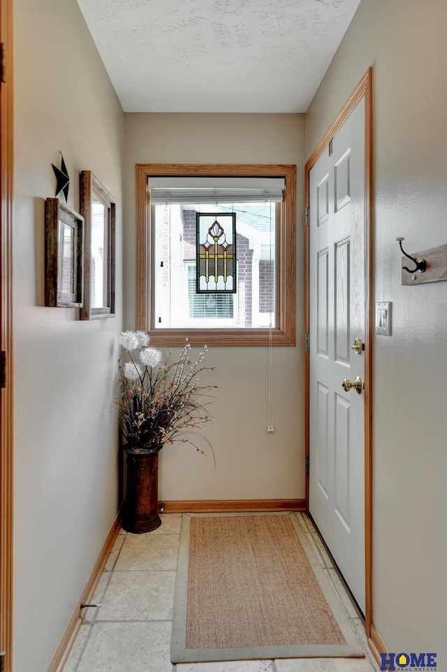 doorway to outside featuring baseboards and a textured ceiling