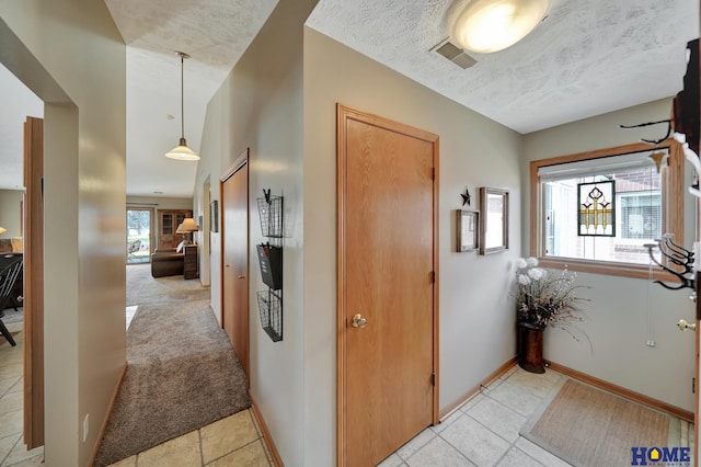 hall featuring baseboards, light colored carpet, visible vents, and a textured ceiling