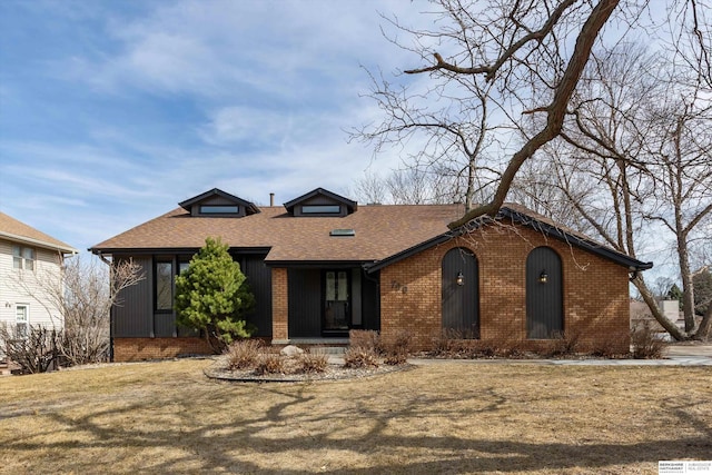 view of front of property featuring brick siding, roof with shingles, and a front lawn