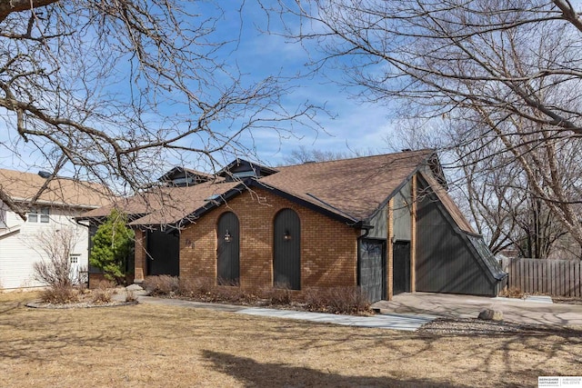 view of front of property with brick siding, a front lawn, fence, concrete driveway, and roof with shingles