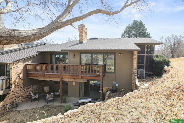 back of property with central AC unit, a shingled roof, a chimney, and a patio area