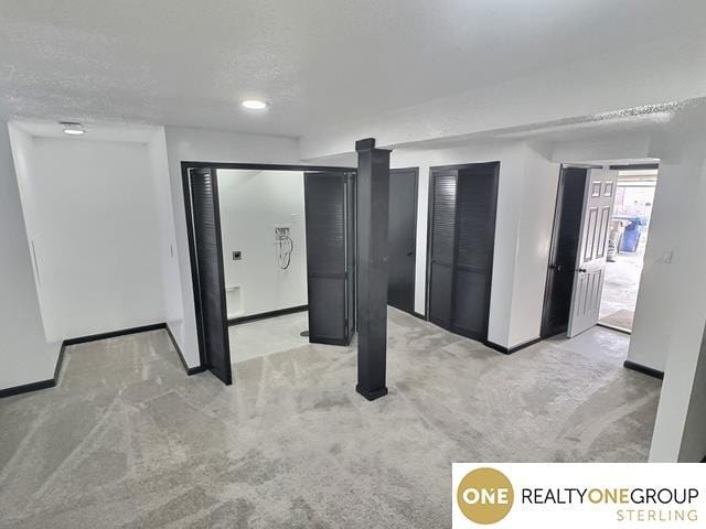 below grade area featuring light colored carpet, a textured ceiling, and baseboards