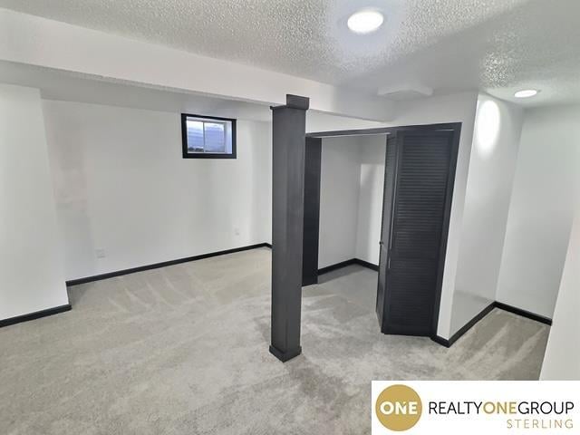 below grade area featuring carpet flooring, a textured ceiling, and baseboards