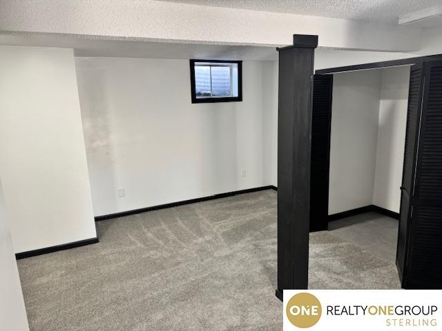 basement featuring carpet flooring, baseboards, and a textured ceiling