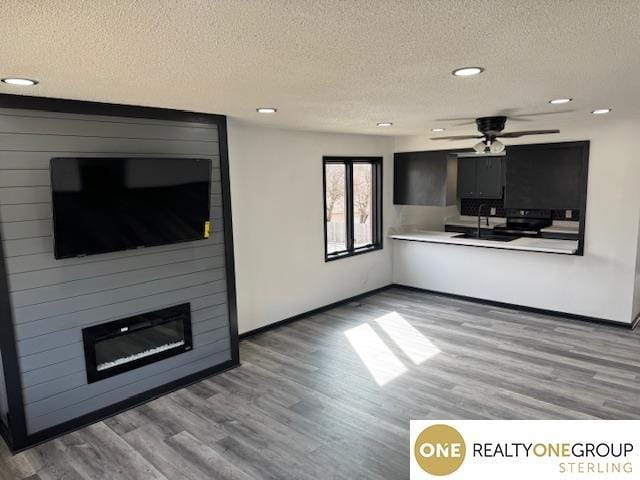 unfurnished living room featuring a textured ceiling, a large fireplace, baseboards, and wood finished floors