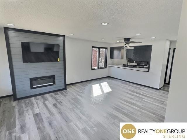 unfurnished living room featuring a textured ceiling, a large fireplace, a ceiling fan, and wood finished floors